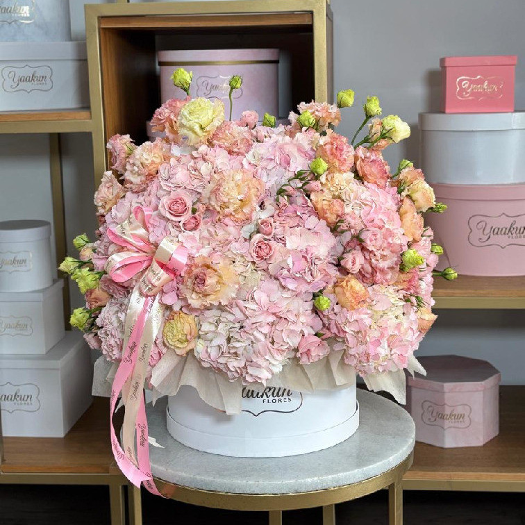 Caja blanca circular con hortensias y lisianthus en tonos rosas