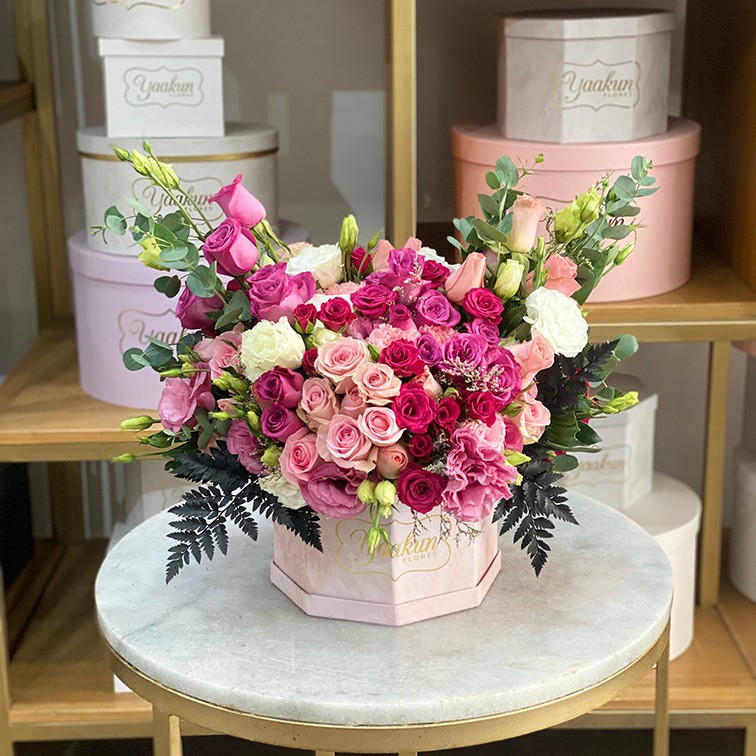 Caja octagonal rosa con 75 rosas en tonos rositas, fucsias, morados & follajes finos.